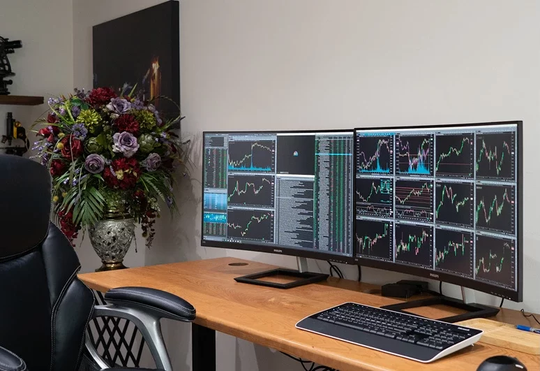 A professional day trading computer setup featuring dual monitors displaying stock market charts on a wooden desk.